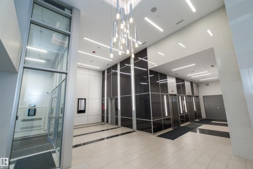 Contemporary lobby featuring a high ceiling, a striking multi-tiered chandelier, recessed linear lighting, and polished floor tiles with contrasting borders - #1201 10238 103 St Nw, Edmonton, AB - Indoor Photo Showing Other Room