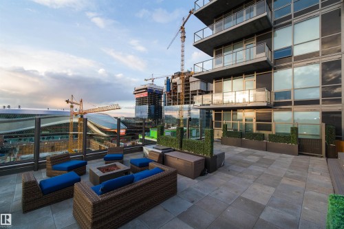 Expansive rooftop patio featuring large format paver flooring, glass panel railings, and integrated planter boxes with artificial greenery - #1201 10238 103 St Nw, Edmonton, AB - Outdoor With Balcony