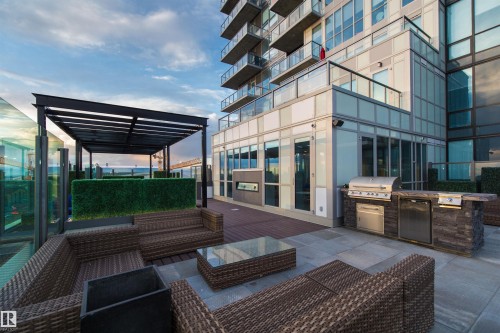 Rooftop patio featuring a large pergola, built-in outdoor kitchen with grill and refrigerator, modern glass railings, and a low-maintenance artificial hedge - #1201 10238 103 St Nw, Edmonton, AB - Outdoor