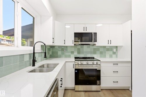 Modern kitchen featuring white cabinetry, light-toned countertops, a stainless steel gas range, and a dual basin sink with a black pull-down faucet - #4 7604 29 Av Nw, Edmonton, AB - Indoor Photo Showing Kitchen With Double Sink