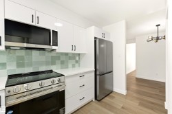 Contemporary kitchen featuring white cabinetry with matte black hardware, stainless steel appliances, a light-toned tile backsplash, and light wood-finish flooring - 