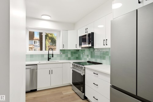 Modern kitchen featuring white cabinetry, stainless steel appliances, a green tile backsplash, white countertops, and wood-finish flooring - #4 7604 29 Av Nw, Edmonton, AB - Indoor Photo Showing Kitchen With Upgraded Kitchen