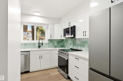 Modern kitchen featuring white cabinetry, stainless steel appliances, a green tile backsplash, white countertops, and wood-finish flooring - 