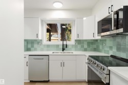 Contemporary kitchen with white cabinetry, light countertops, and a mint green tile backsplash - 