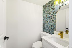 Powder room with a mosaic tile accent wall, white vanity with an integrated sink, gold-tone faucet, and an arched mirror - 