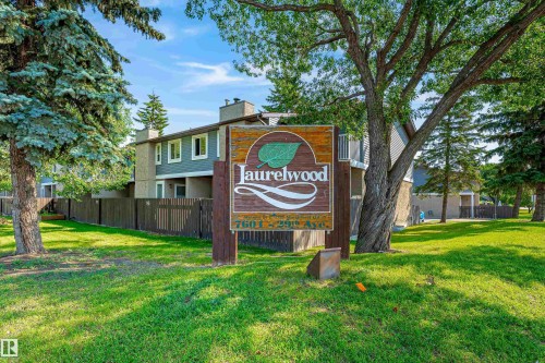 Community entrance sign with established landscaping, featuring mature trees and green lawn space - #4 7604 29 Av Nw, Edmonton, AB - Outdoor
