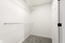 Walk-in closet featuring white wire shelving, white walls, gray carpet, white baseboards, and a white paneled door with black hardware - 