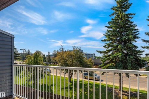 Balcony featuring white railings and siding, overlooking a street with mature trees and a grassy area - #4 7604 29 Av Nw, Edmonton, AB - Outdoor With Balcony