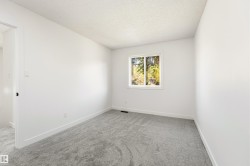 Neutral-toned room featuring a window with white trim, light grey patterned carpeting, crisp white walls, and matching white baseboards - 