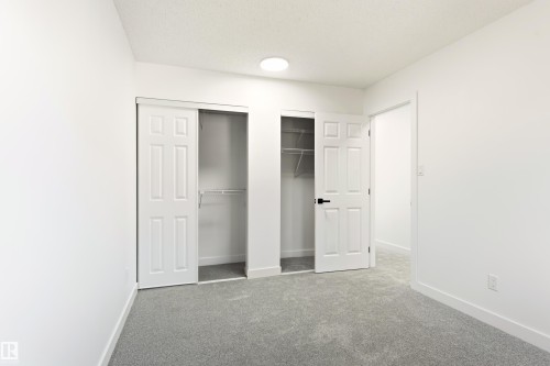 Room featuring light gray carpeting, white walls, and a built-in closet with sliding panel doors and wire shelving - #4 7604 29 Av Nw, Edmonton, AB - Indoor Photo Showing Other Room