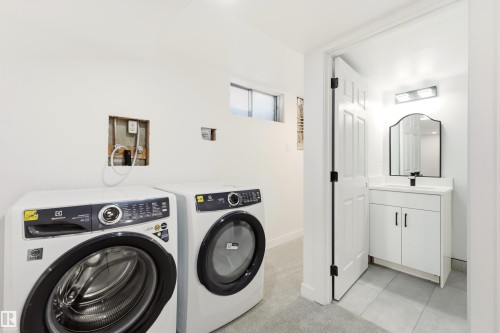 Dedicated laundry area featuring a front-load washer and dryer, complemented by a nearby bathroom with a white vanity and a framed mirror - #4 7604 29 Av Nw, Edmonton, AB - Indoor Photo Showing Laundry Room