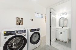 Dedicated laundry area featuring a front-load washer and dryer, complemented by a nearby bathroom with a white vanity and a framed mirror - 