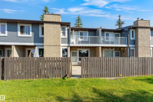 Townhome exterior featuring blue horizontal siding, stucco accents, and a private fenced yard with a wooden gate - #4 7604 29 Av Nw, Edmonton, AB - Outdoor With Balcony