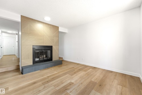 Spacious living area featuring a wood-finish flooring, recessed lighting, and a contemporary fireplace with a geometric wood-paneled surround and a stone-finish hearth - #4 7604 29 Av Nw, Edmonton, AB - Indoor Photo Showing Other Room With Fireplace