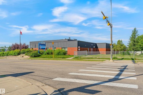 Brick and gray facade building with a prominent sign, flagpole, and mature landscaping - #4 7604 29 Av Nw, Edmonton, AB - Outdoor With View