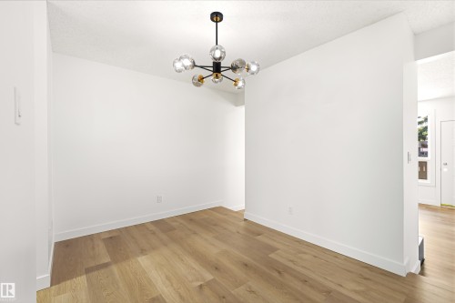 Room featuring wood-finish flooring, crisp white walls, and a contemporary multi-bulb chandelier - #4 7604 29 Av Nw, Edmonton, AB - Indoor Photo Showing Other Room