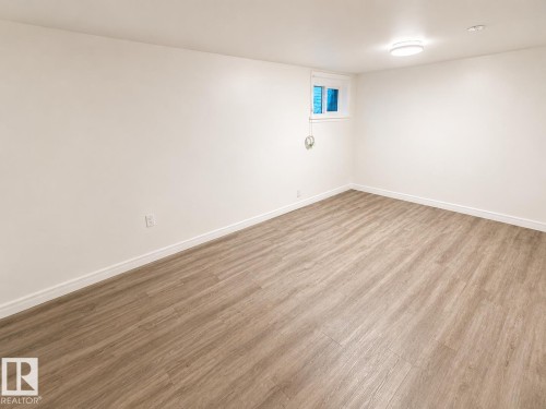 Spacious interior featuring wood-finish flooring, crisp white walls, white baseboards, a single window, and a ceiling-mounted light fixture - 12235 104 Street Nw, Edmonton, AB - Indoor Photo Showing Other Room