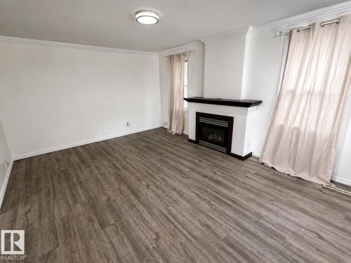 Open living space featuring wood-finish flooring, a built-in fireplace with a dark mantel, white baseboards, and crown molding - 12235 104 Street Nw, Edmonton, AB - Indoor With Fireplace