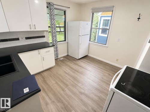 Kitchen featuring wood-finish flooring, white cabinetry with brushed nickel hardware, dark countertops, a white subway tile backsplash with black accent tiles, and dual windows - 12235 104 Street Nw, Edmonton, AB - Indoor Photo Showing Kitchen With Double Sink