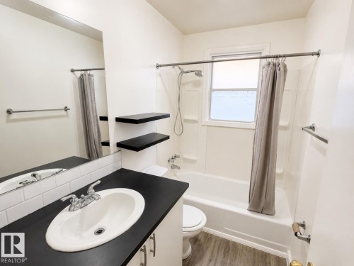 Bathroom featuring a white subway tile backsplash, dark countertop, floating shelves, and a full bathtub with an overhead shower - 12235 104 Street Nw, Edmonton, AB - Indoor Photo Showing Bathroom