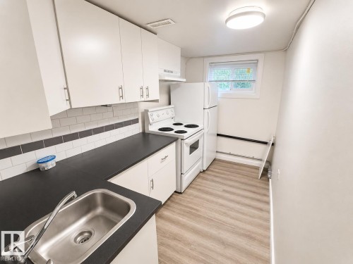 Compact kitchen featuring white cabinetry with silver-tone hardware, black countertops, and a white subway tile backsplash with a dark accent stripe - 12235 104 Street Nw, Edmonton, AB - Indoor Photo Showing Kitchen