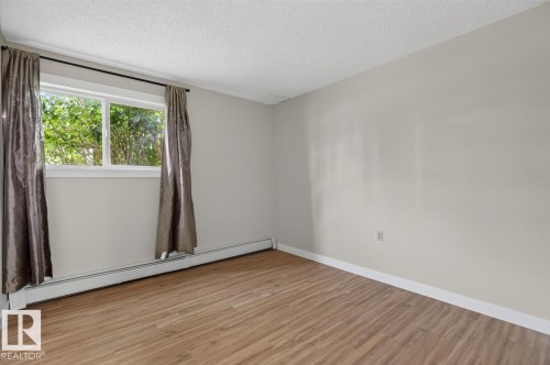 Spacious room featuring wood-finish flooring, light-toned wall paint, and a window providing natural illumination - #5 11265 31 Av Nw, Edmonton, AB - Indoor Photo Showing Other Room