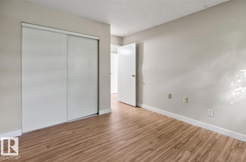 Spacious room featuring wood-finish flooring, light neutral wall paint, and a textured ceiling - #5 11265 31 Av Nw, Edmonton, AB - Indoor Photo Showing Other Room