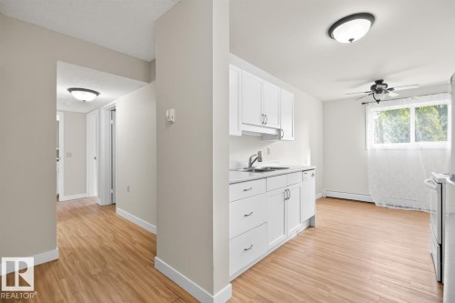 Kitchenette featuring white cabinetry, a stainless steel sink, and wood-finish flooring - #5 11265 31 Av Nw, Edmonton, AB - Indoor Photo Showing Other Room