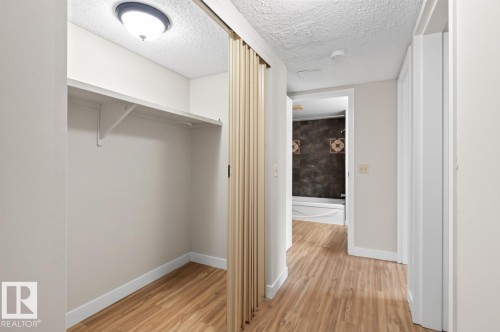 Hallway featuring wood-finish flooring, white baseboards, and a built-in closet with shelving and a bi-fold door - #5 11265 31 Av Nw, Edmonton, AB - Indoor Photo Showing Other Room