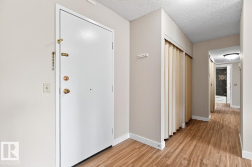Entryway featuring wood-finish flooring, a white entry door with brass hardware, and a built-in closet with bifold doors - #5 11265 31 Av Nw, Edmonton, AB - Indoor Photo Showing Other Room