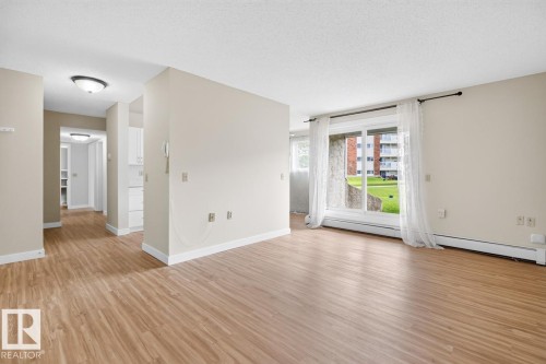 Spacious room featuring wood-finish flooring, light neutral wall tones, and a large sliding glass door - #5 11265 31 Av Nw, Edmonton, AB - Indoor
