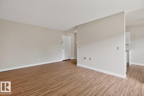 Spacious living area featuring wood-finish flooring, light neutral wall tones, and white baseboards - #5 11265 31 Av Nw, Edmonton, AB - Indoor Photo Showing Other Room