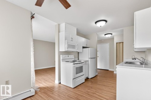 Compact kitchen featuring wood-finish flooring, white cabinetry, and a full suite of white appliances - #5 11265 31 Av Nw, Edmonton, AB - Indoor Photo Showing Kitchen With Double Sink