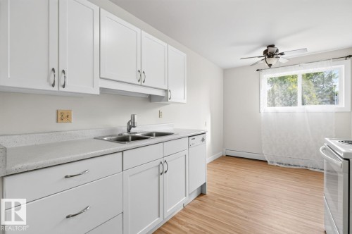 Kitchen featuring white cabinetry, light-toned countertops, a double-basin stainless steel sink, and wood-finish flooring - #5 11265 31 Av Nw, Edmonton, AB - Indoor Photo Showing Kitchen With Double Sink