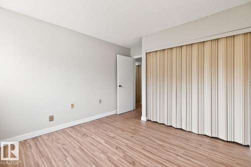 Interior room featuring wood-finish flooring, light-toned walls, white baseboards, and a neutral-colored accordion closet door - #5 11265 31 Av Nw, Edmonton, AB - Indoor Photo Showing Other Room