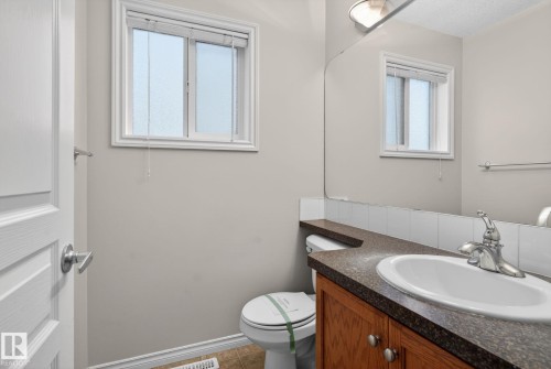 Bathroom featuring a single window, a wood-finish vanity with a built-in sink, a speckled countertop, and a large wall-mounted mirror - 96 Dalquist Bay, Leduc, AB - Indoor Photo Showing Bathroom