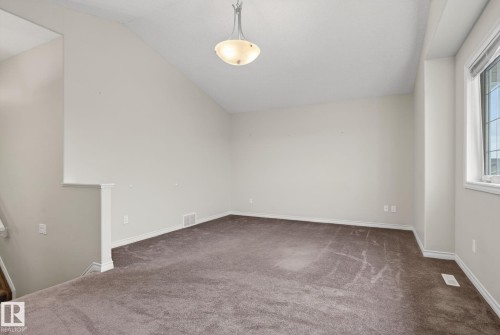 Spacious carpeted room featuring a sloped ceiling, contemporary semi-flush mount light fixture, and a window with white trim - 96 Dalquist Bay, Leduc, AB - Indoor Photo Showing Other Room