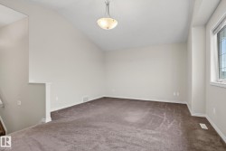 Spacious carpeted room featuring a sloped ceiling, contemporary semi-flush mount light fixture, and a window with white trim - 