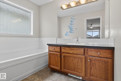 Bathroom featuring a built-in bathtub, frosted privacy window, wood-finish vanity with ample storage, a dark countertop, and a large wall-mounted mirror - 96 Dalquist Bay, Leduc, AB - Indoor Photo Showing Bathroom