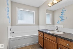 Bathroom featuring a white bathtub with chrome fixtures, a frosted window, and a wood-finish vanity with an integrated sink and dark countertop - 