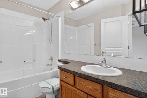 Bathroom featuring a white bathtub and shower combination with a curved shower curtain rod, a wood-finish vanity with a dark speckled countertop, and an oval undermount sink with chrome fixtures - 96 Dalquist Bay, Leduc, AB - Indoor Photo Showing Bathroom
