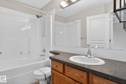Bathroom featuring a white bathtub and shower combination with a curved shower curtain rod, a wood-finish vanity with a dark speckled countertop, and an oval undermount sink with chrome fixtures - 