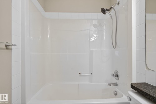 White bathtub and shower combination unit featuring a chrome showerhead with hose, a single-handle faucet, and an integrated grab bar - 96 Dalquist Bay, Leduc, AB - Indoor Photo Showing Bathroom