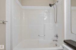 White bathtub and shower combination unit featuring a chrome showerhead with hose, a single-handle faucet, and an integrated grab bar - 