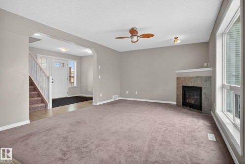 Spacious living area featuring neutral-toned carpeting, a corner-mounted fireplace with a tiled surround, and multiple windows - 96 Dalquist Bay, Leduc, AB - Indoor With Fireplace