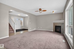 Spacious living area featuring neutral-toned carpeting, a corner-mounted fireplace with a tiled surround, and multiple windows - 