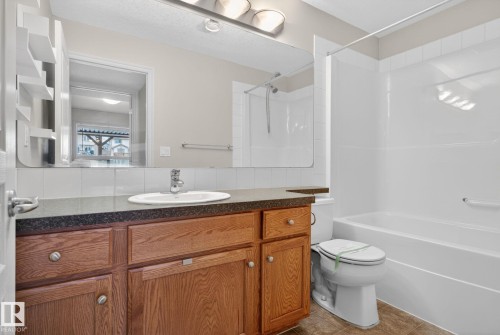 Bathroom featuring a wood-finish vanity with an integrated sink, dark countertop, and a white tile backsplash - 96 Dalquist Bay, Leduc, AB - Indoor Photo Showing Bathroom