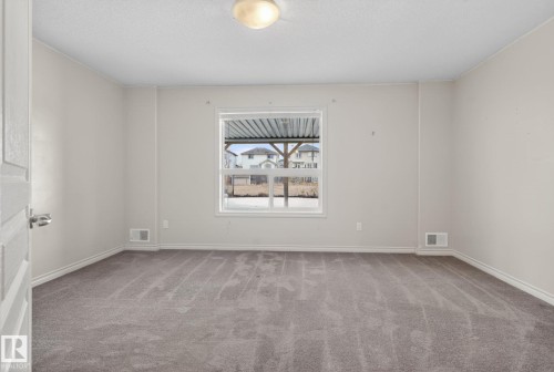 Spacious bedroom with neutral wall finishes, carpeted flooring in a warm gray tone, and abundant natural light from a large double-hung window - 96 Dalquist Bay, Leduc, AB - Indoor Photo Showing Other Room