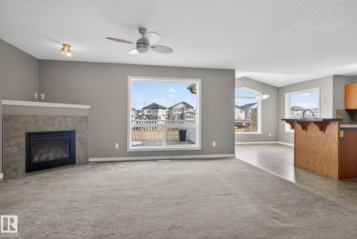 Carpeted living area featuring a tile-surround fireplace with mantel, a large window overlooking a deck, and a ceiling fan - 96 Dalquist Bay, Leduc, AB - Indoor Photo Showing Living Room With Fireplace