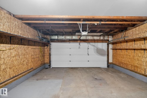 Spacious garage featuring a white paneled overhead door, exposed beam ceiling with mechanical systems, concrete flooring, and cork-faced side walls providing insulation and durability - 96 Dalquist Bay, Leduc, AB - Indoor Photo Showing Garage